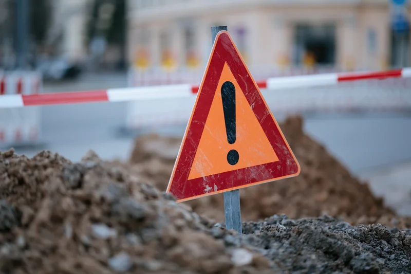 Triangular warning sign with exclamation mark in dirt at construction site