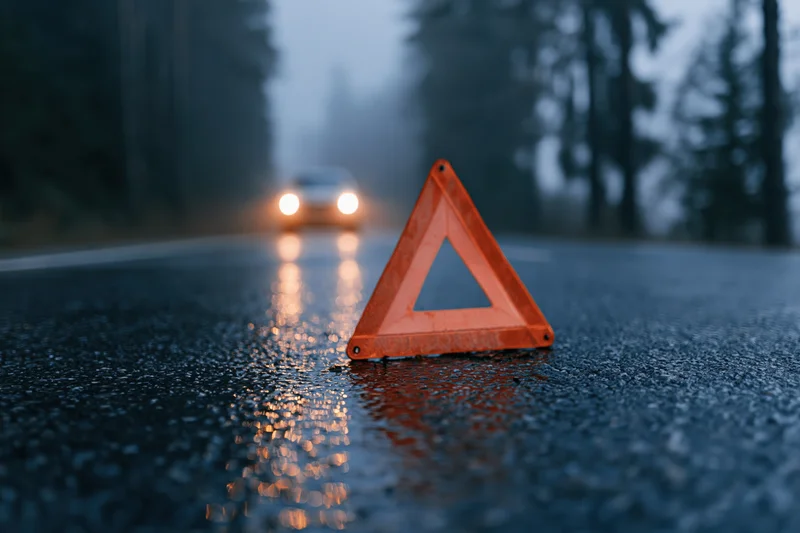 Orange reflective emergency triangle on wet road at night with approaching car headlights