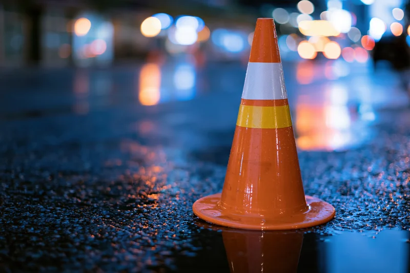 Orange traffic cone with reflective bands standing on wet pavement at night in a city street