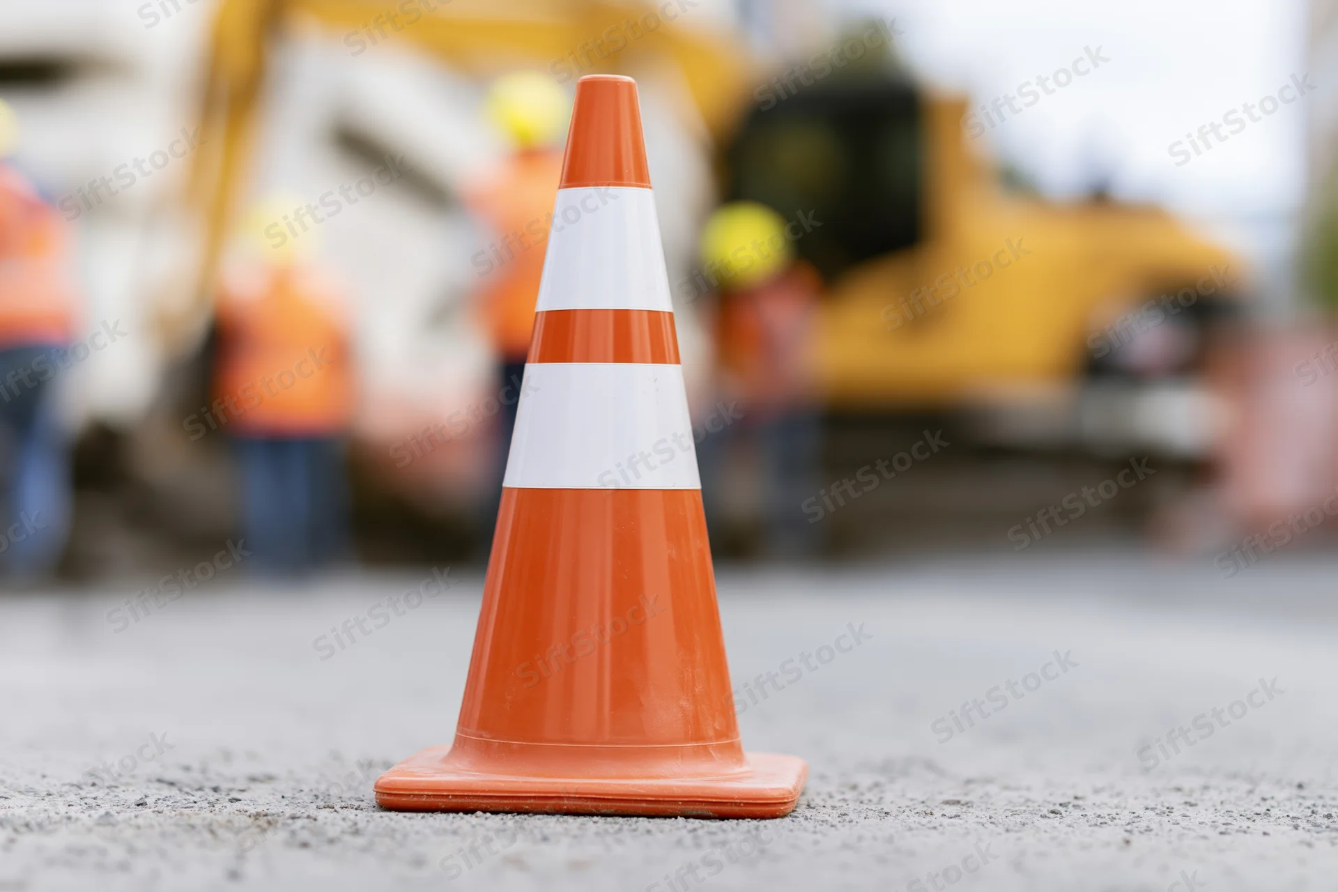 Orange traffic cone with white reflective bands on asphalt at construction site