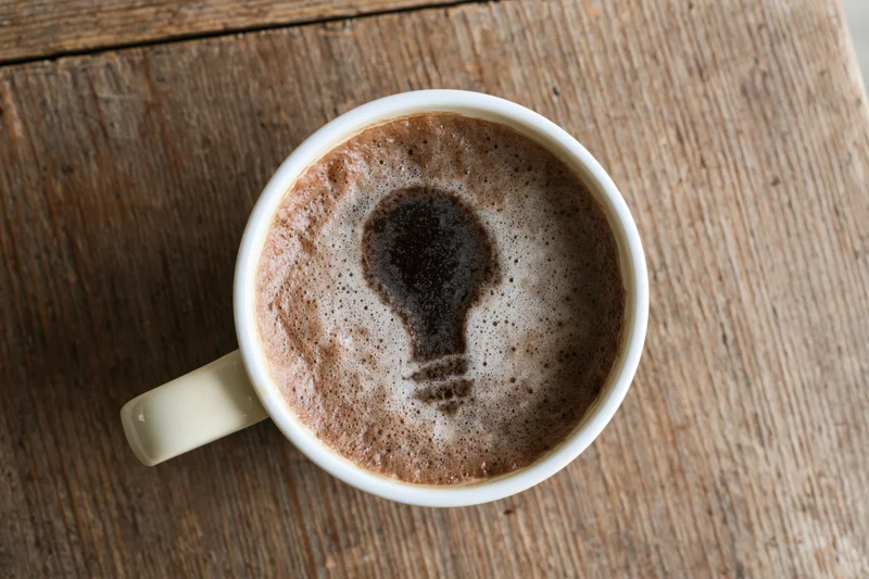 White ceramic coffee mug with lightbulb-shaped foam on wooden table