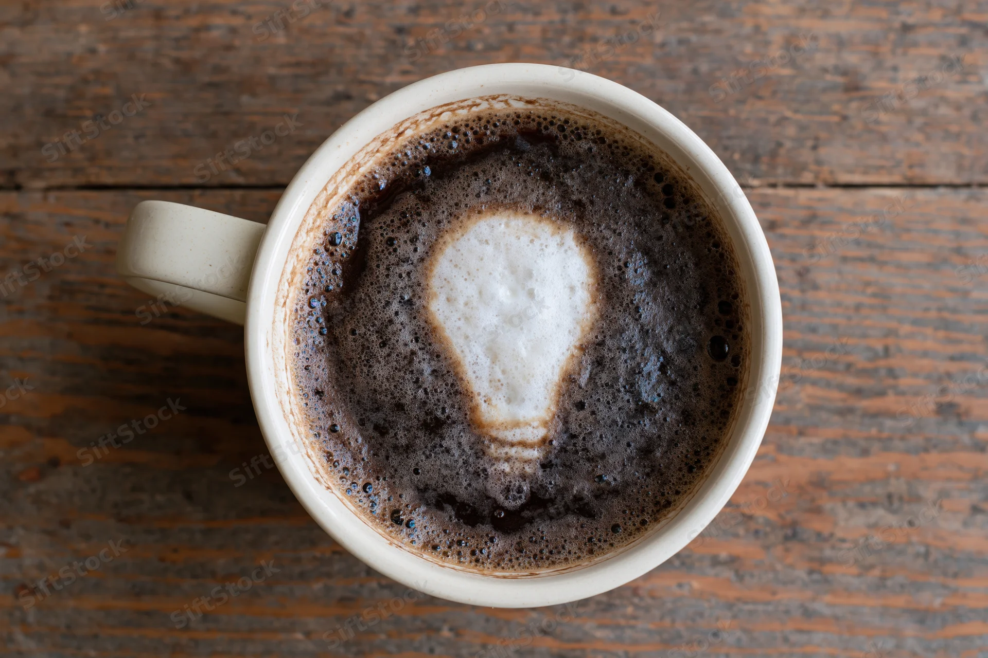 White ceramic coffee mug with lightbulb-shaped foam art on wooden table