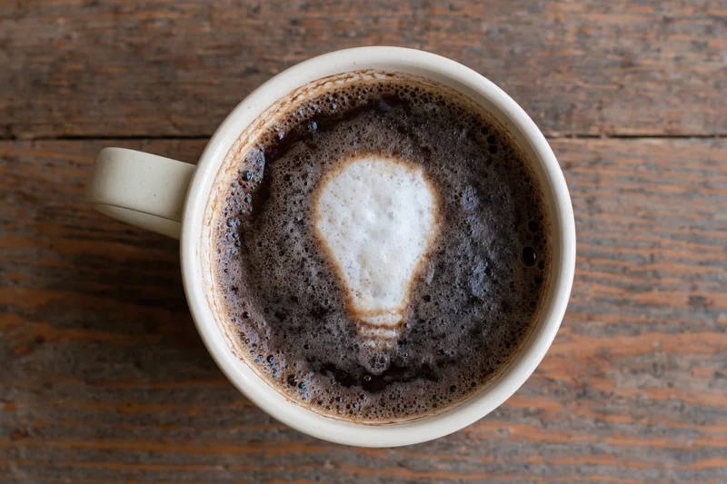 White ceramic coffee mug with lightbulb-shaped foam art on wooden table