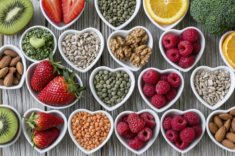 Heart-shaped bowls filled with fresh fruits vegetables nuts seeds arranged on wooden surface in flat lay overhead view