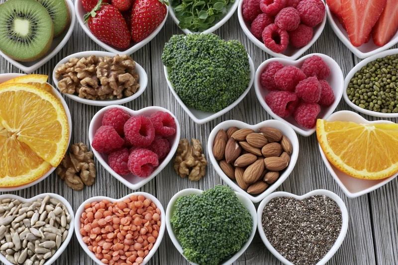 Heart-shaped bowls filled with fresh fruits vegetables seeds and nuts arranged on wooden table