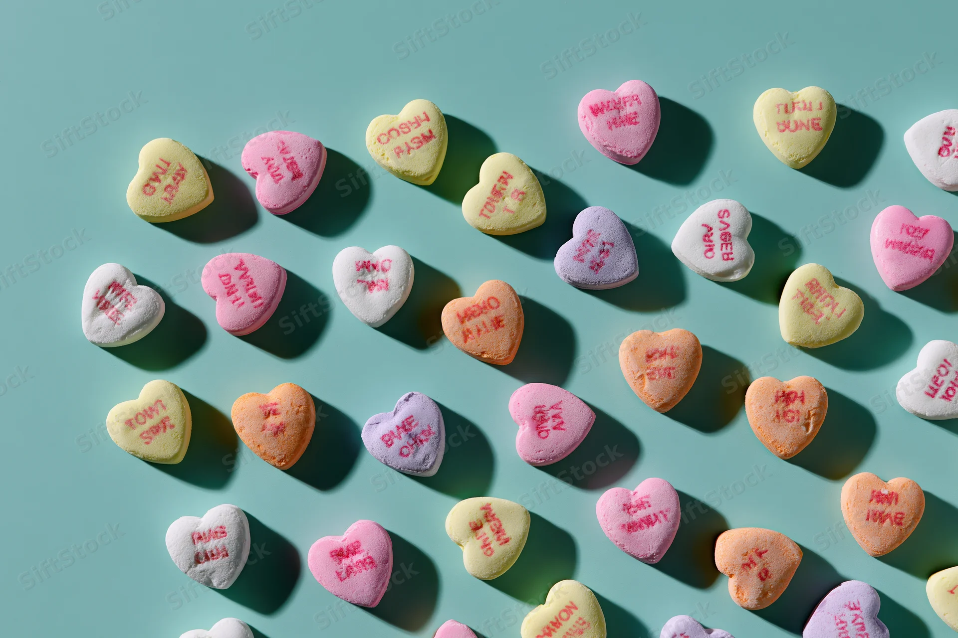 Pastel heart-shaped candies with messages arranged in loose grid on teal background