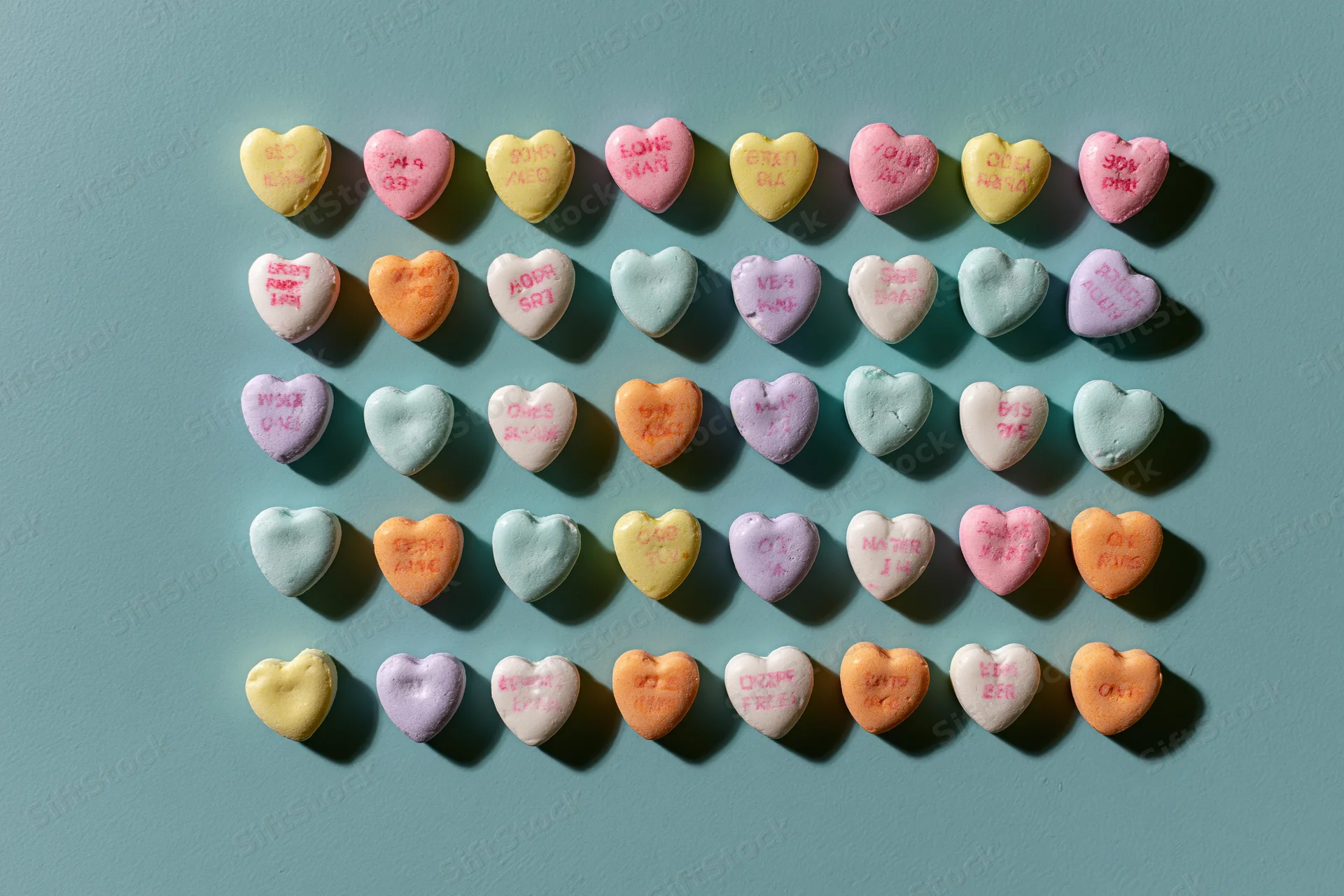 Pastel conversation heart candies arranged in a loose grid on a teal surface