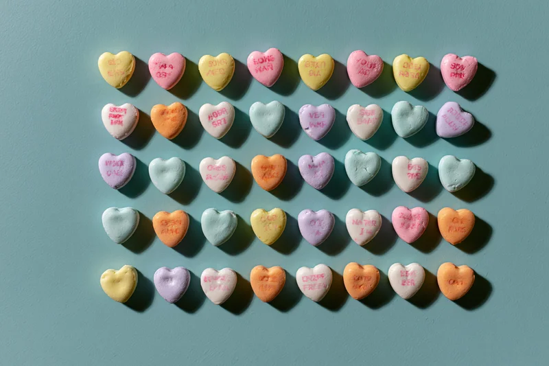 Pastel conversation heart candies arranged in a loose grid on a teal surface