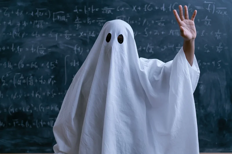 Student in ghost costume raising hand in classroom with math equations on blackboard