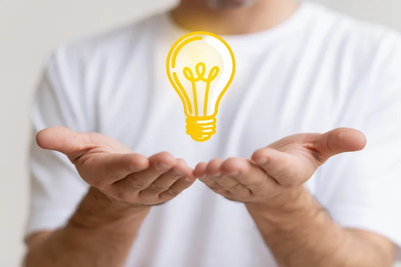 Man holding open cupped hands with glowing yellow lightbulb symbol floating above them