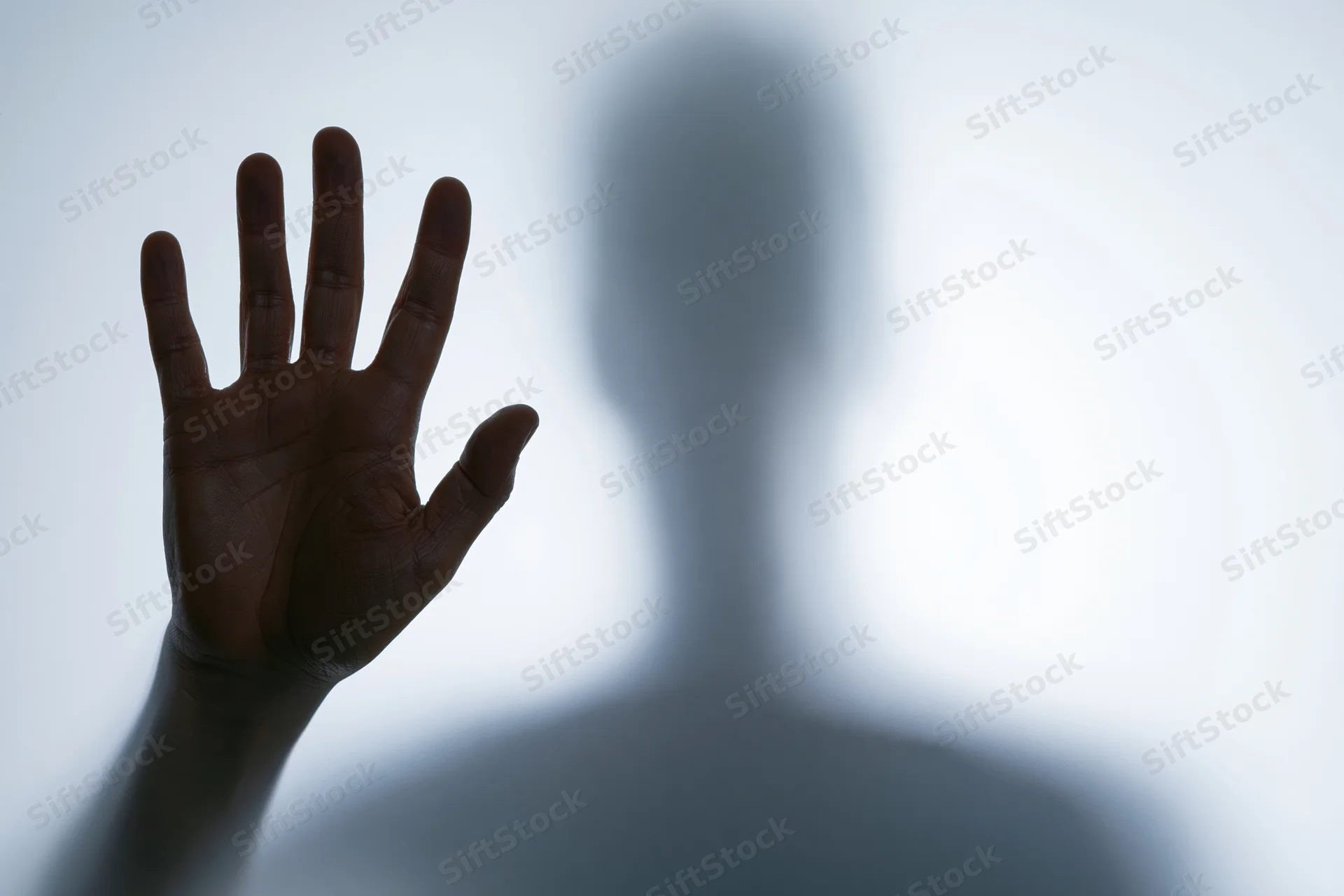 Hand pressed flat against frosted glass with blurred human silhouette behind