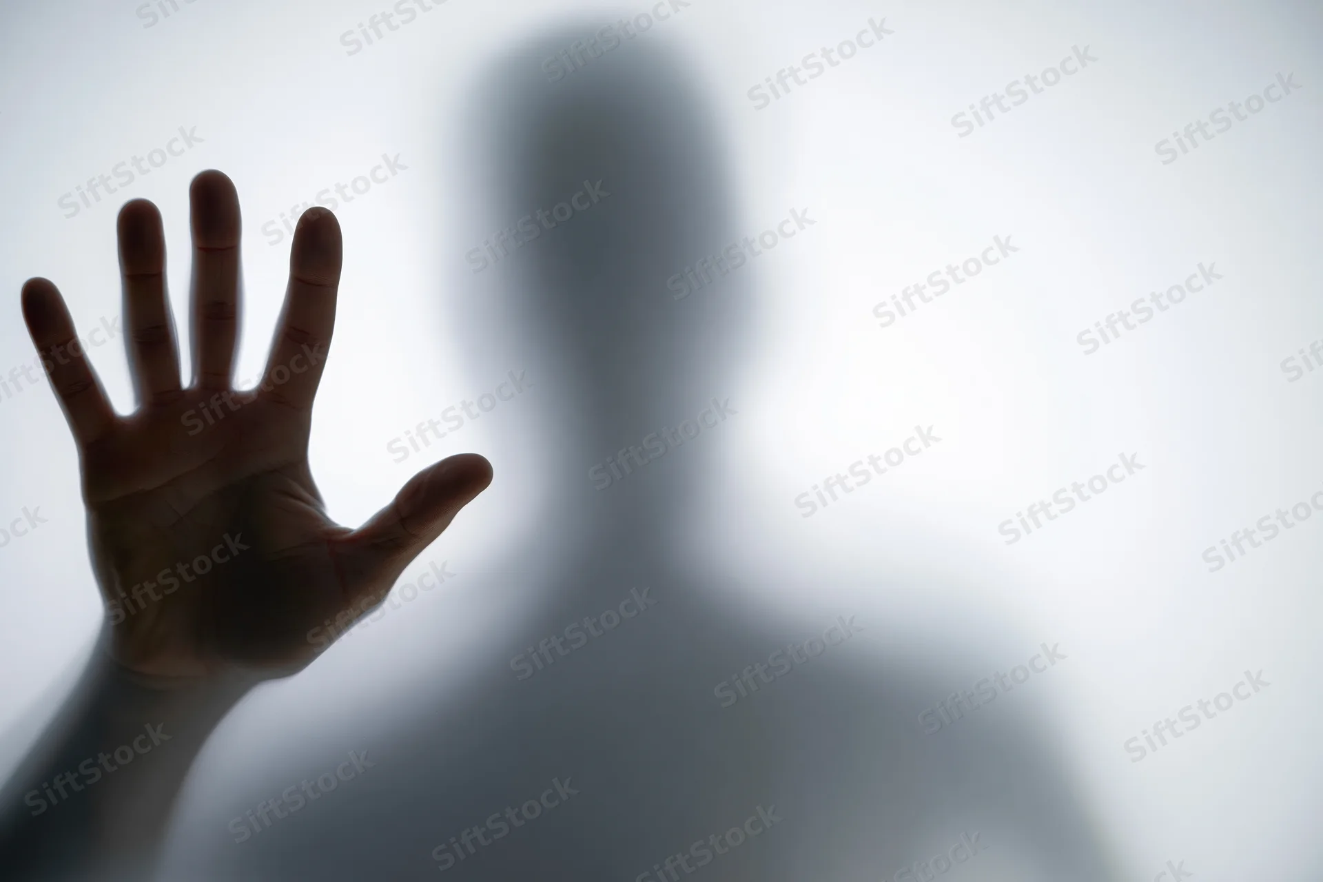 Hand pressed flat against frosted glass with blurred silhouette behind