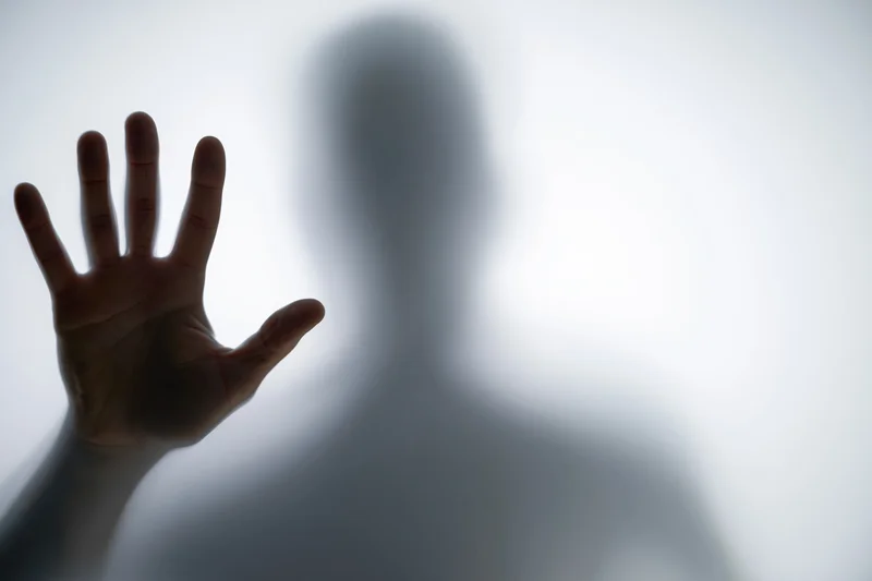Hand pressed flat against frosted glass with blurred silhouette behind