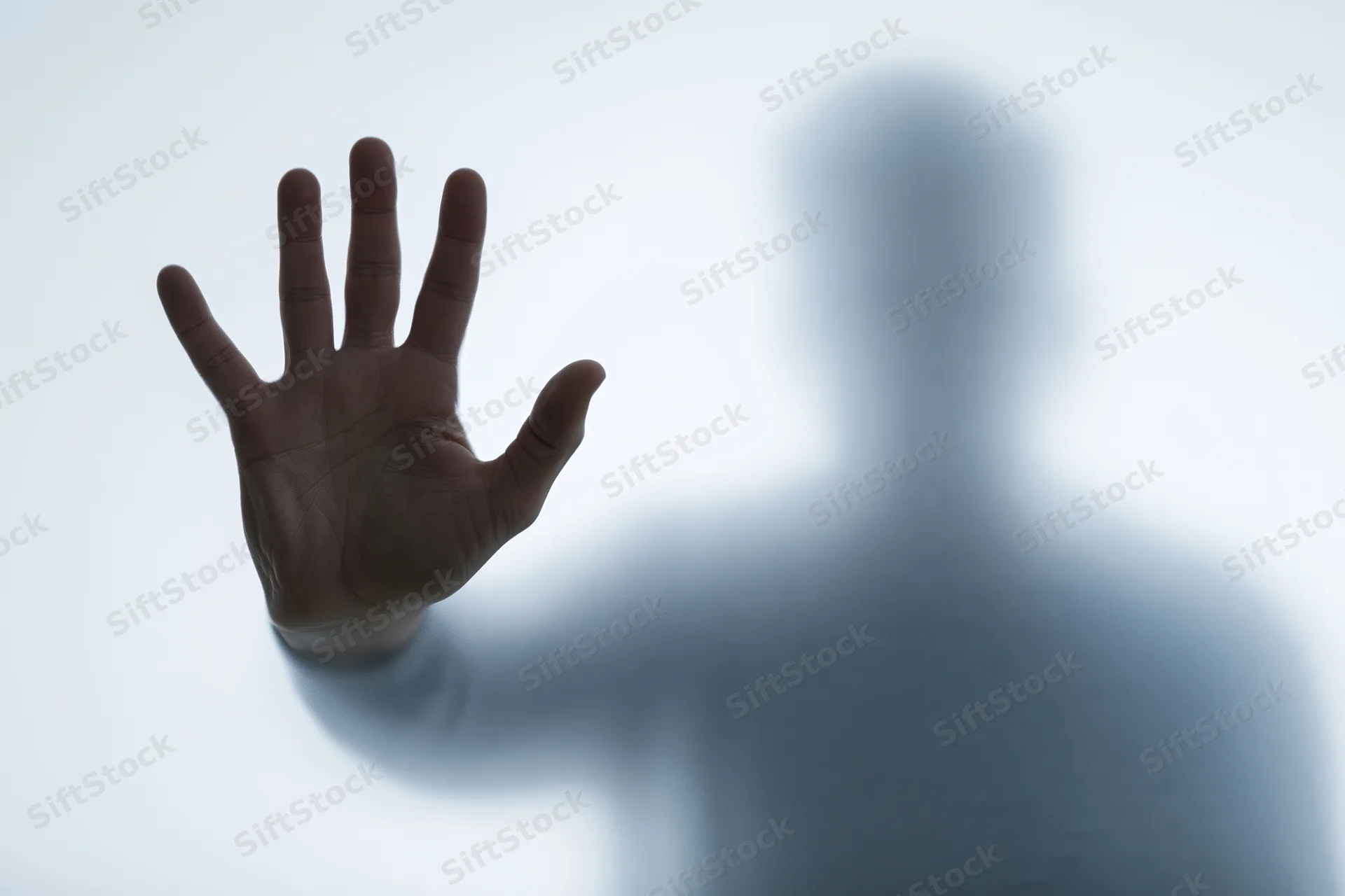 Hand pressed flat against frosted glass with blurred human silhouette behind