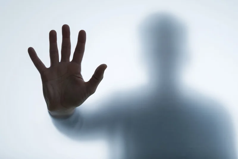 Hand pressed flat against frosted glass with blurred human silhouette behind