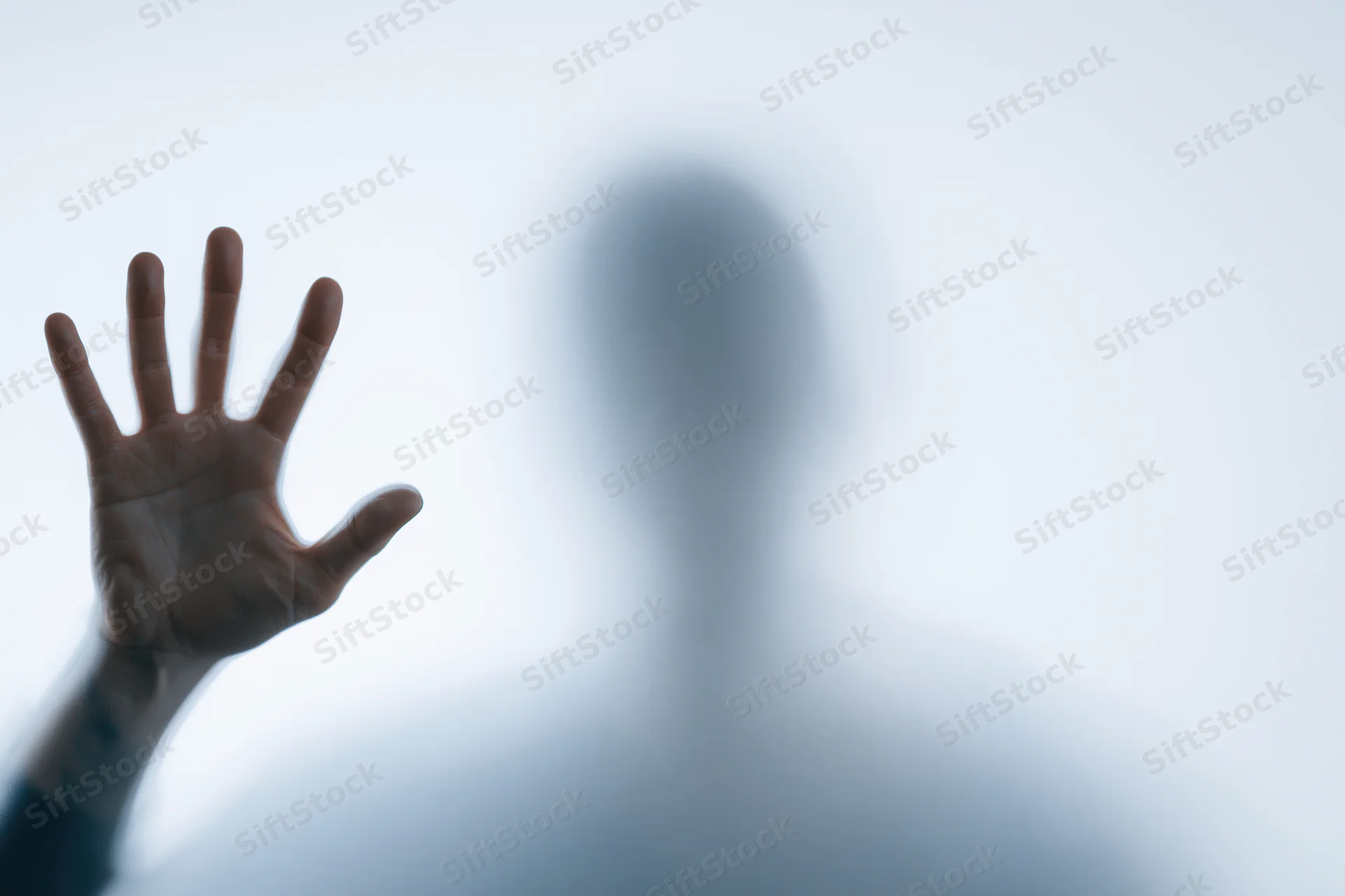 Hand pressed flat against frosted glass with blurred human silhouette behind