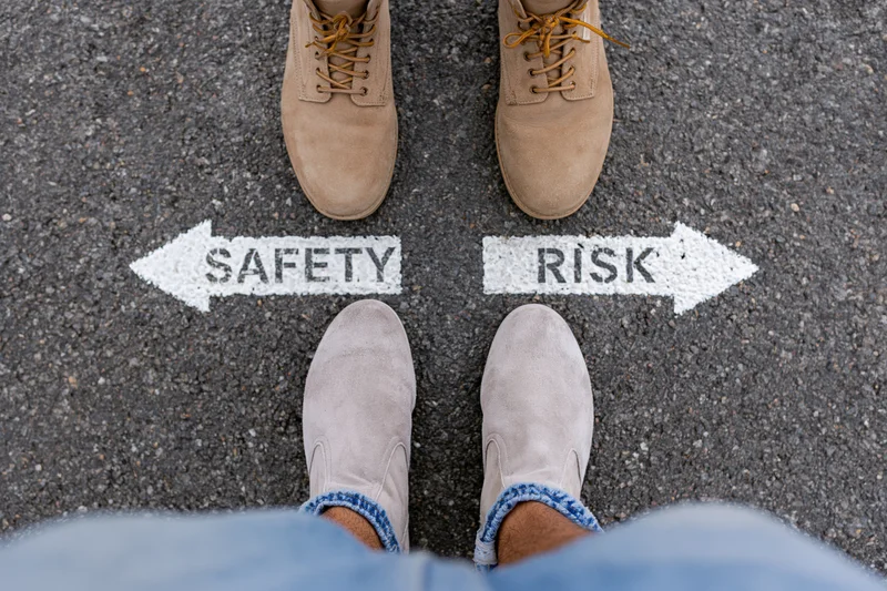 Person standing at crossroads with safety and risk arrows painted on asphalt pavement