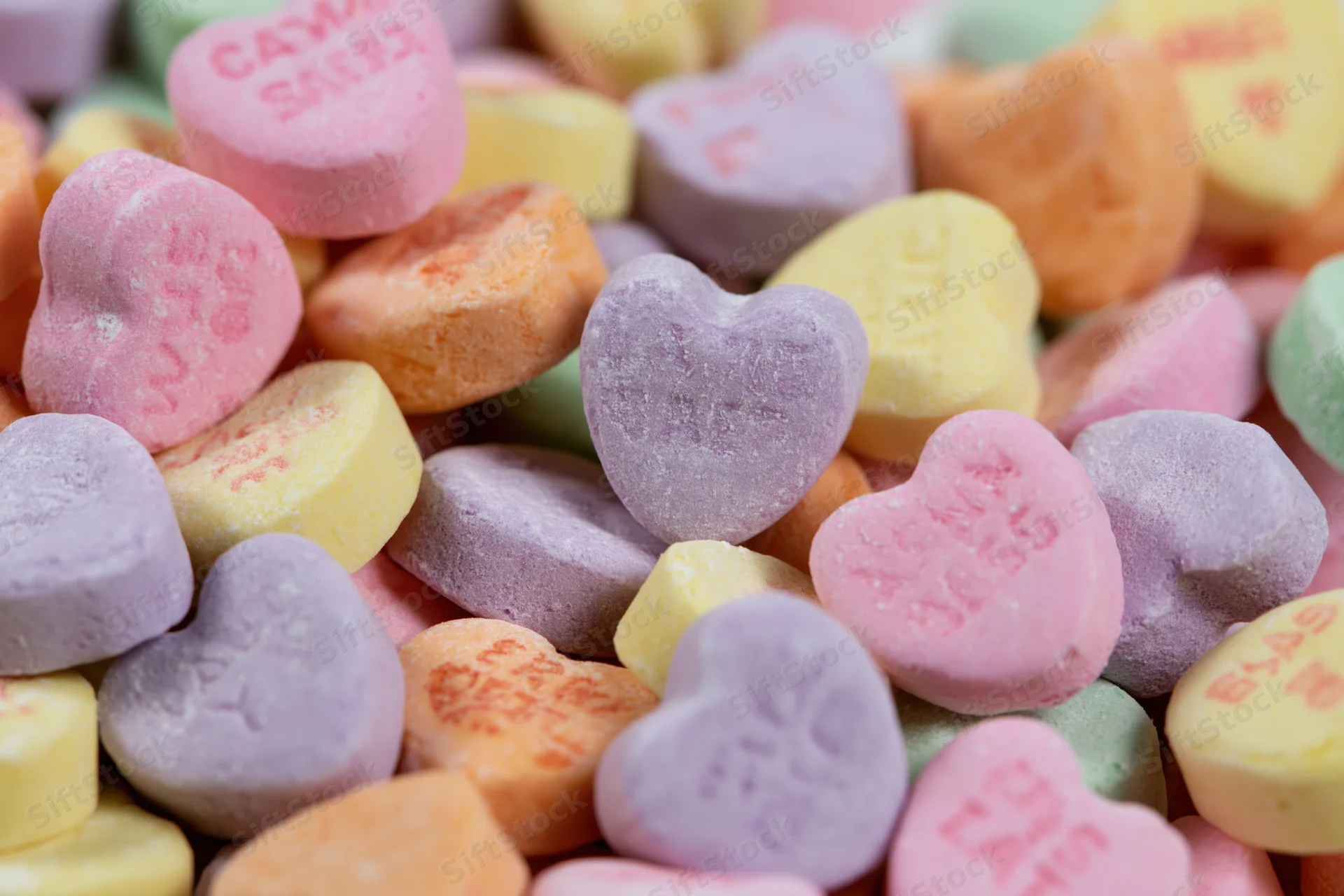 Pile of pastel heart-shaped candies with embossed messages scattered together