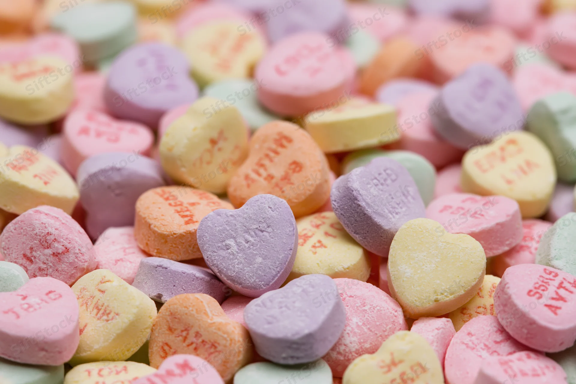 Pile of pastel heart-shaped candies with printed messages scattered closely together