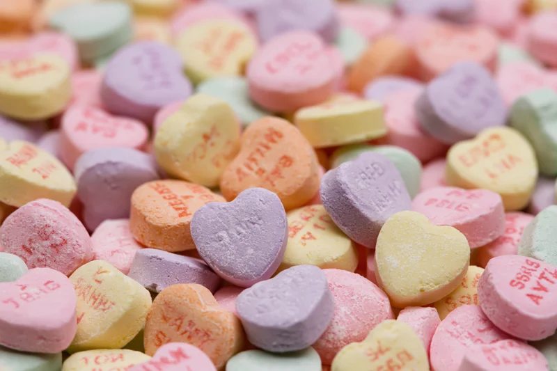 Pile of pastel heart-shaped candies with printed messages scattered closely together