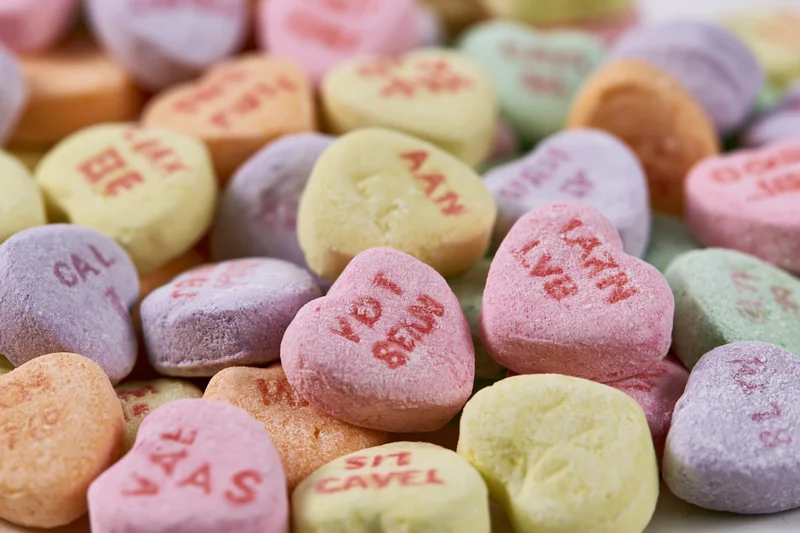 Pile of pastel heart-shaped candies with love messages scattered closely together