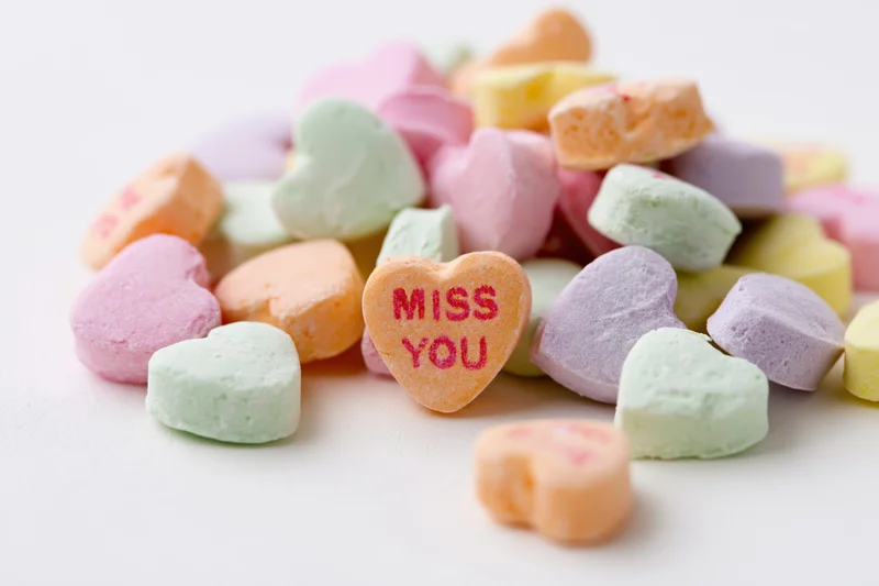Pile of pastel heart-shaped candies with miss you message on white background