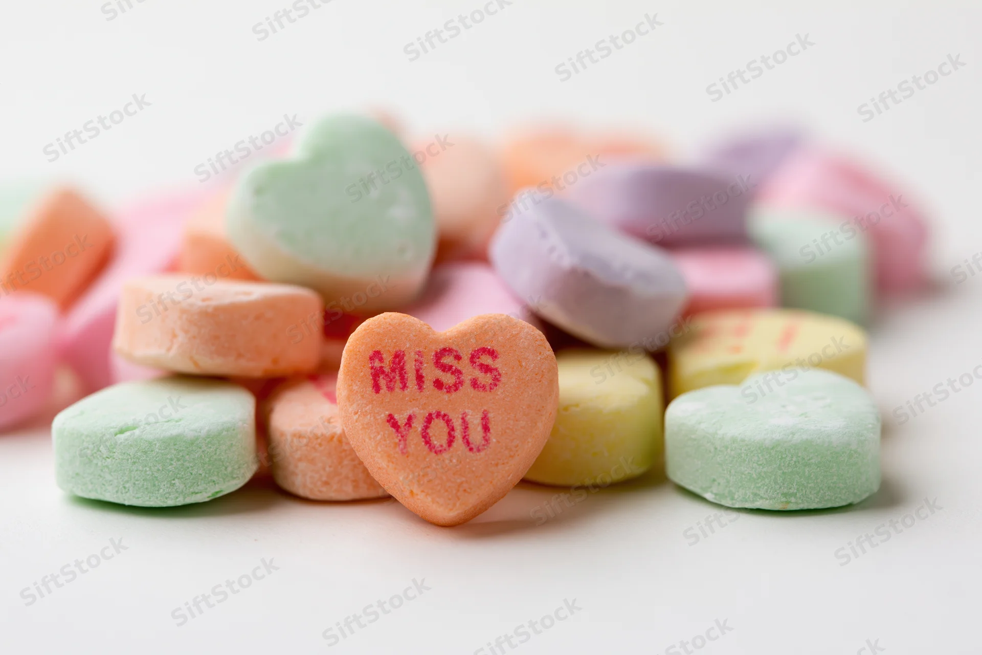 Pile of pastel conversation hearts with miss you message on white background