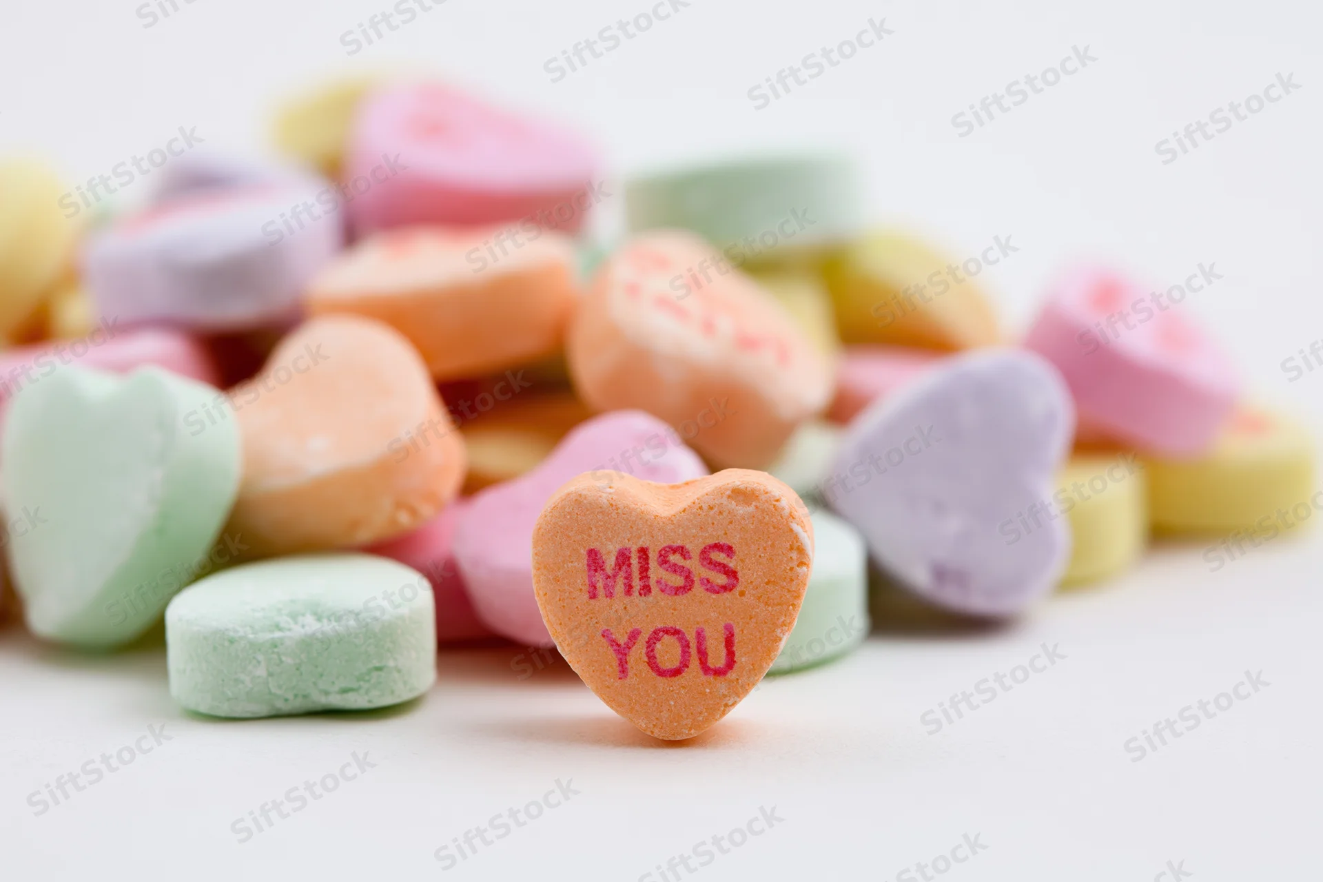 Pile of pastel conversation hearts scattered on white background with one heart reading miss you in focus