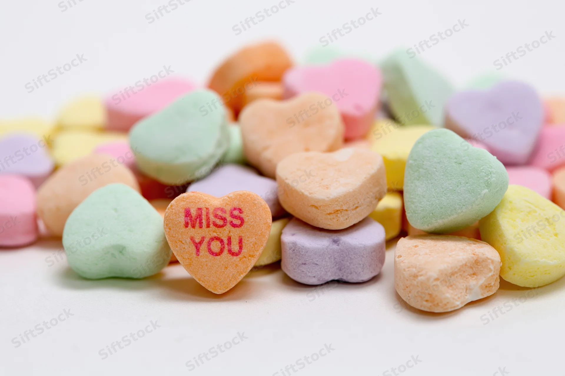 Pile of pastel conversation hearts with miss you message on white background