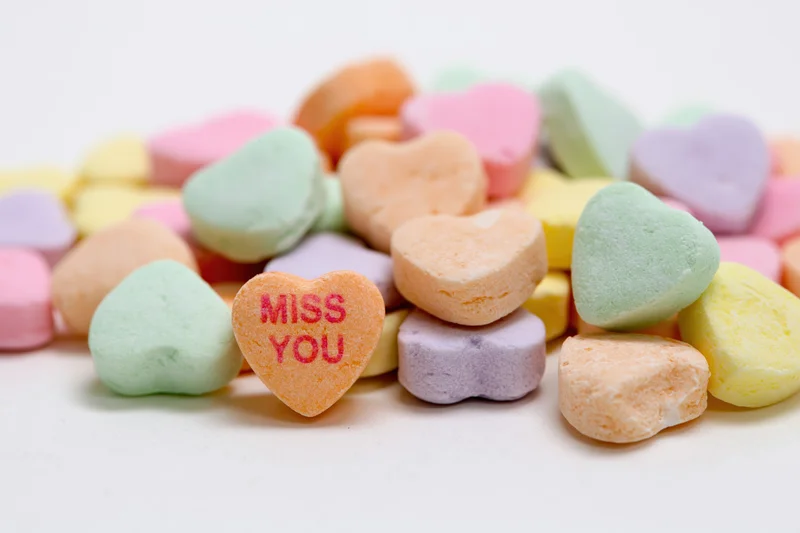 Pile of pastel conversation hearts with miss you message on white background