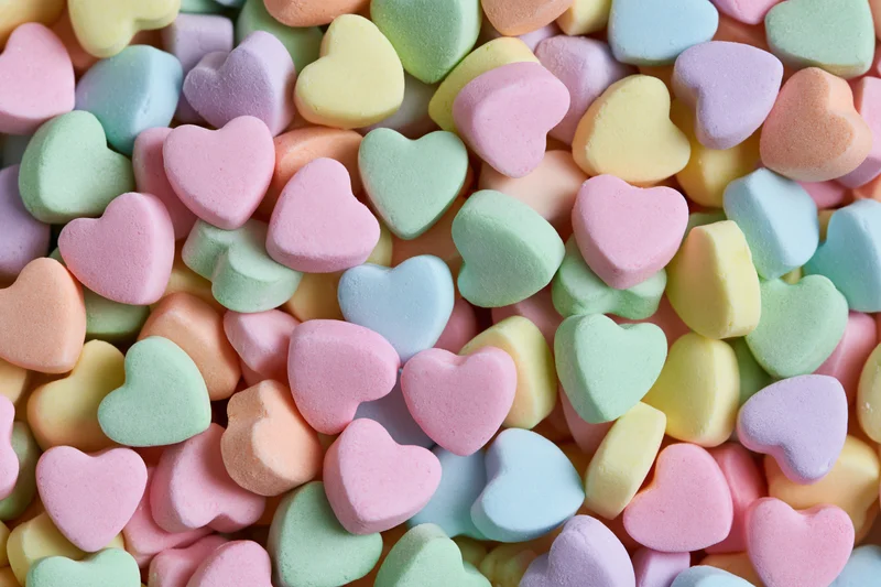 Pastel candy hearts piled together filling the frame