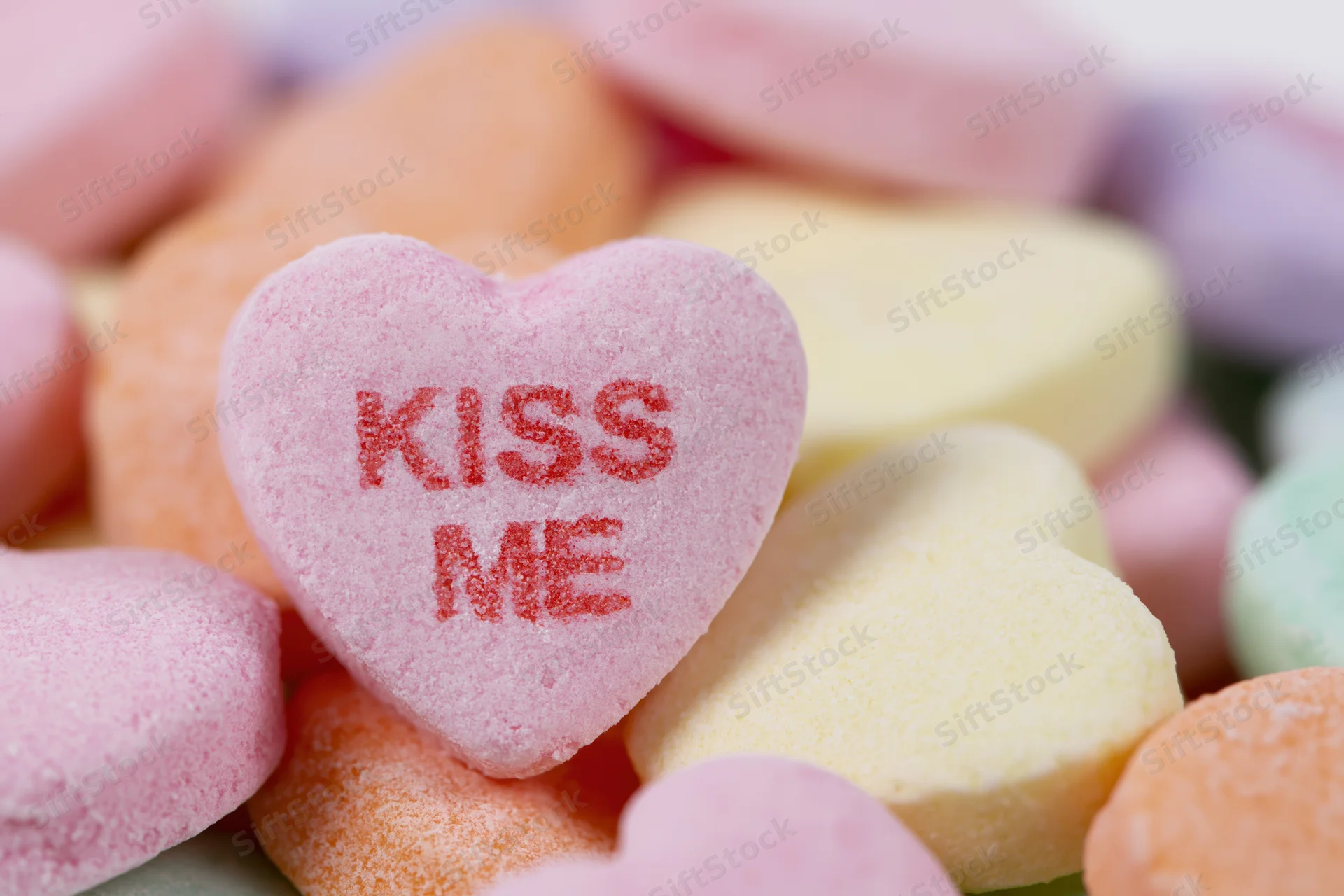 Pink heart-shaped candy with kiss me text among colorful sweets