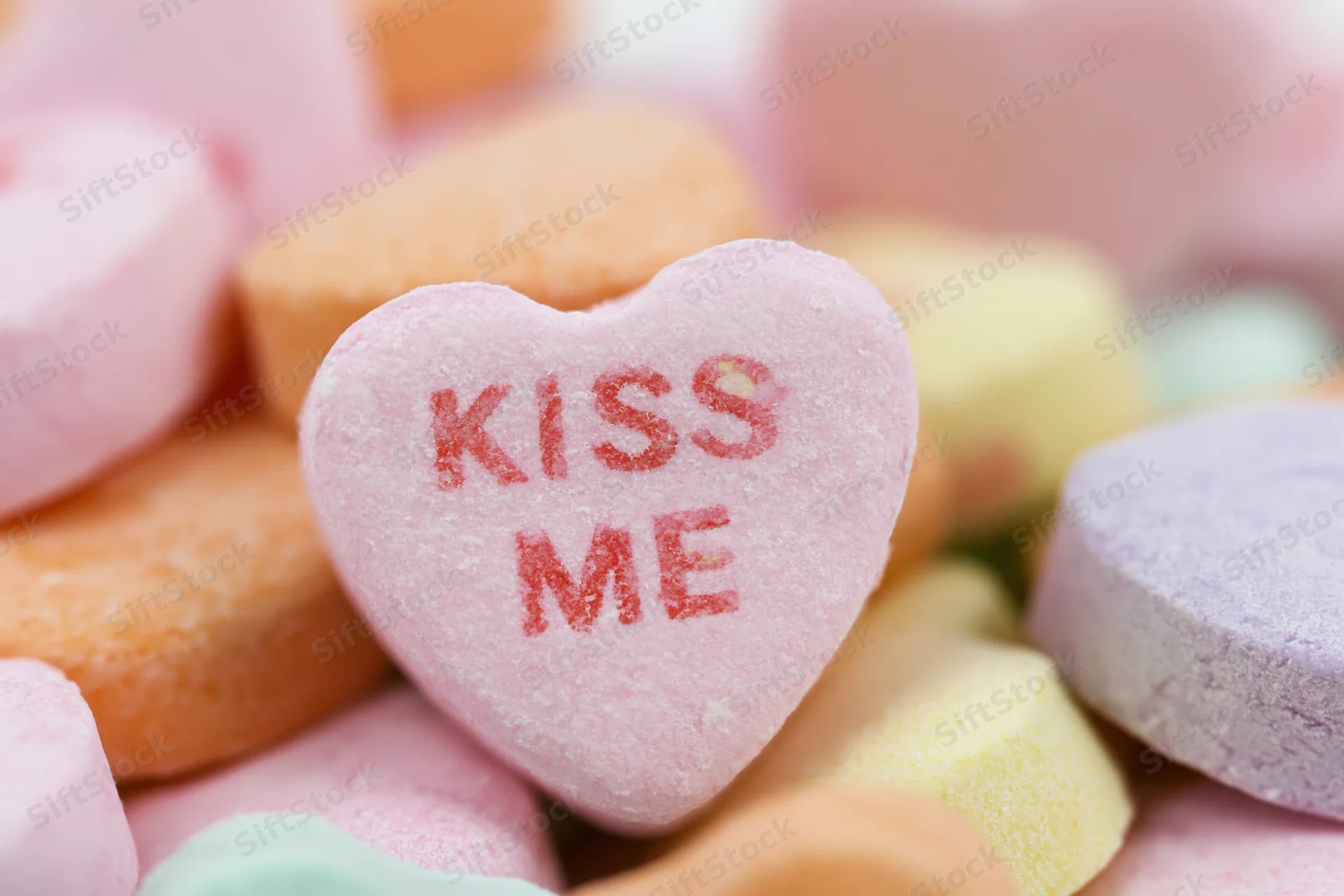 Pink heart-shaped candy with kiss me text among colorful sweets