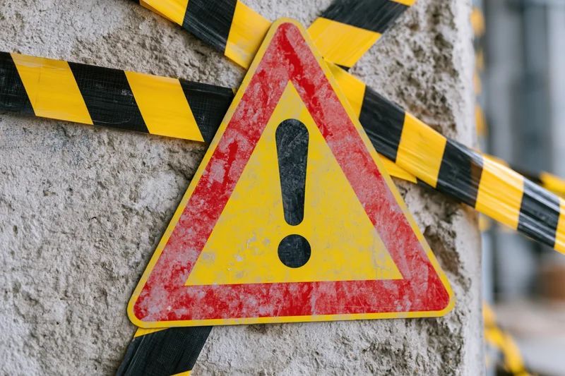 Triangular warning sign with exclamation mark attached to concrete pole with yellow and black caution tape