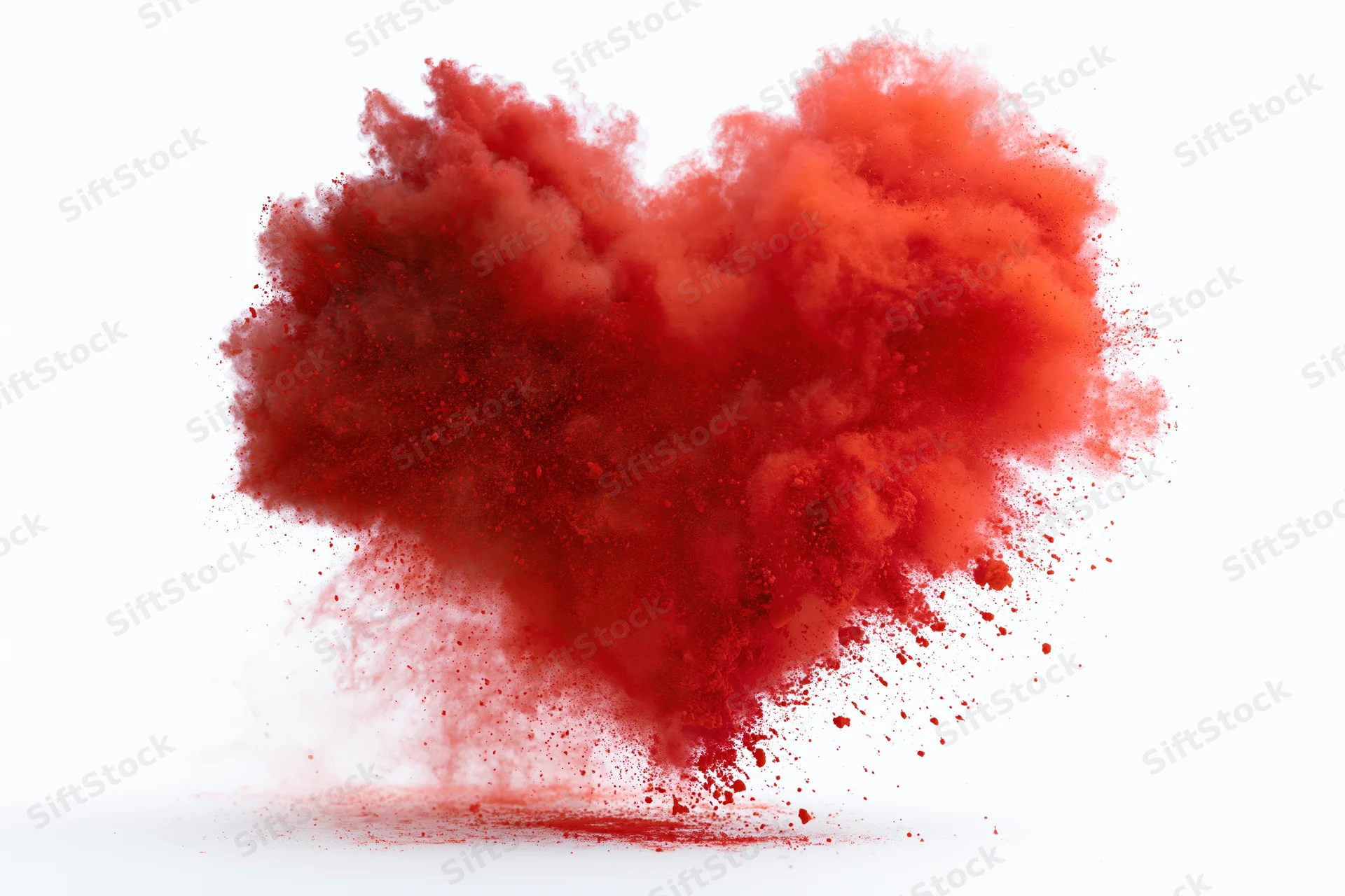 Red powder exploding in heart shape midair against white background