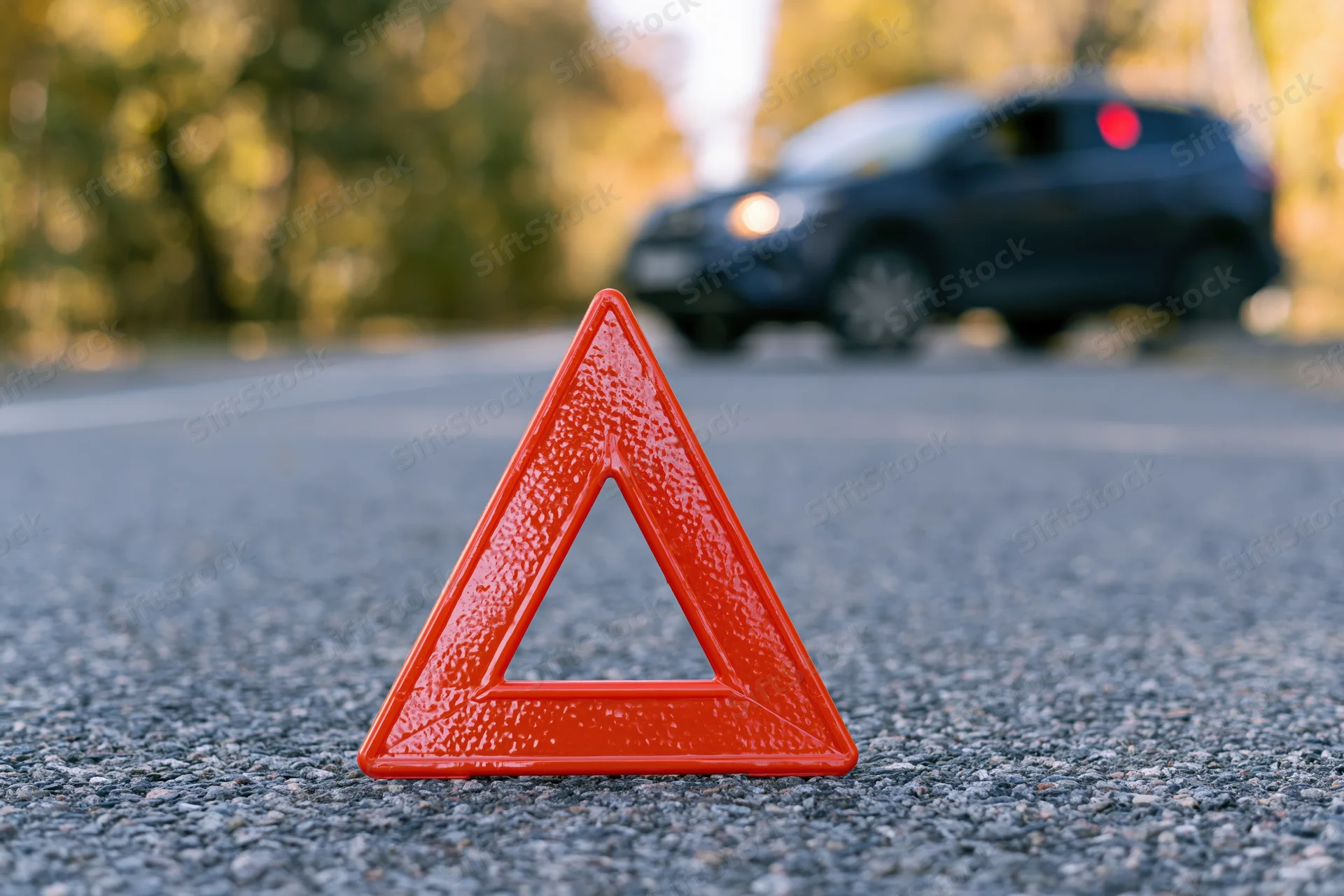 Red emergency warning triangle on asphalt road with car in background