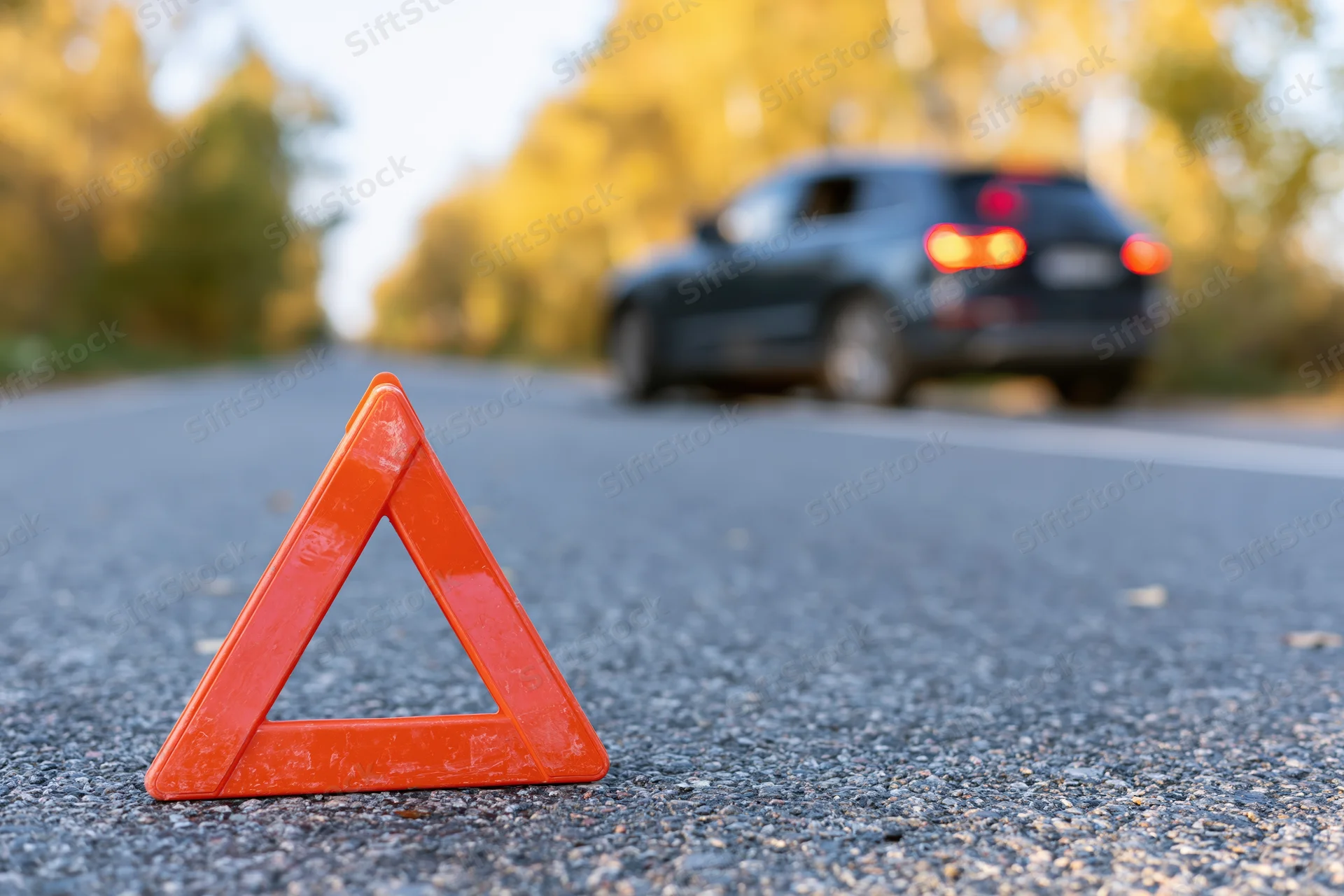 Red emergency warning triangle on asphalt road with car in background