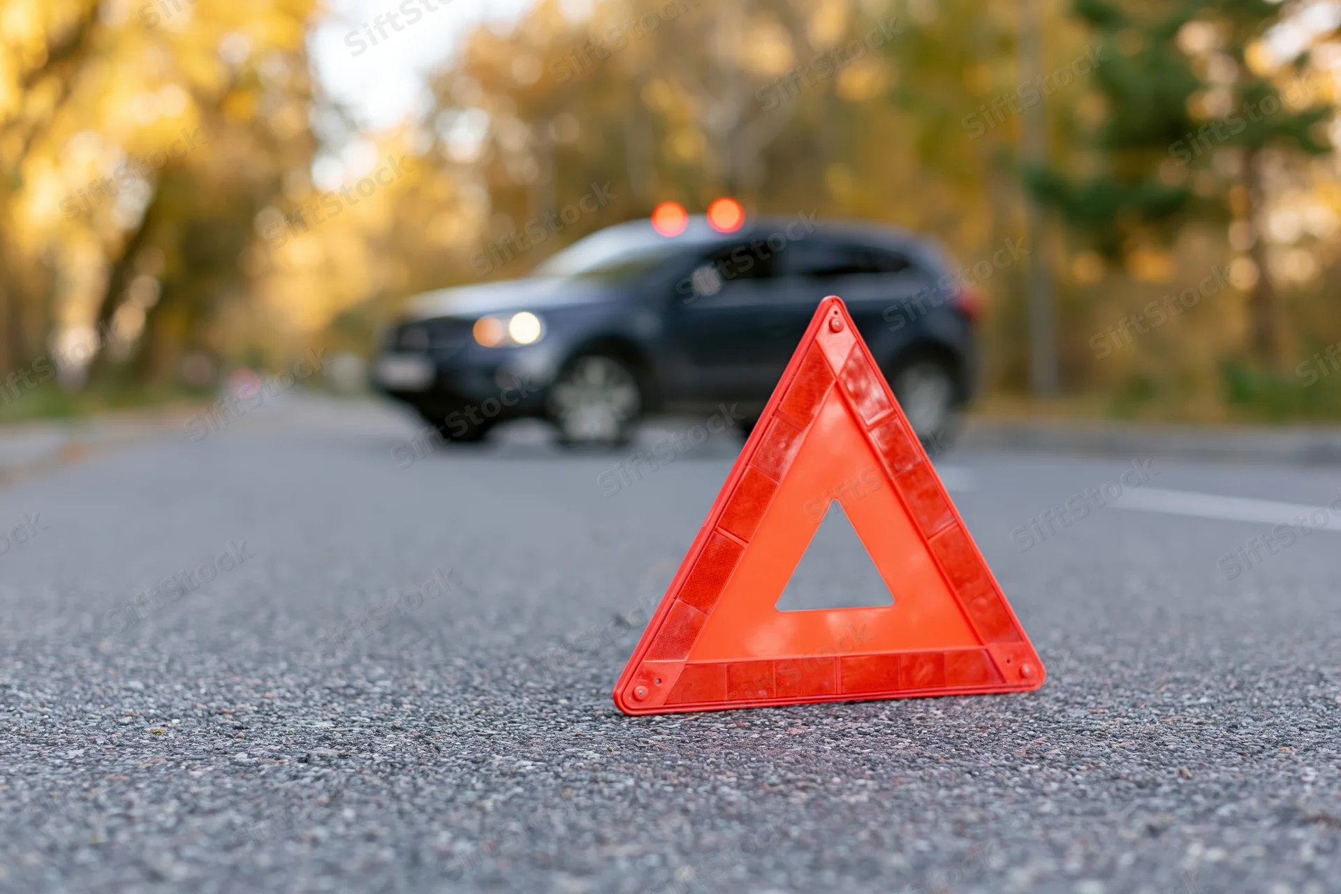 Red emergency warning triangle on asphalt road with car in background