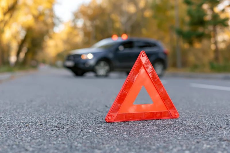 Red emergency warning triangle on asphalt road with car in background