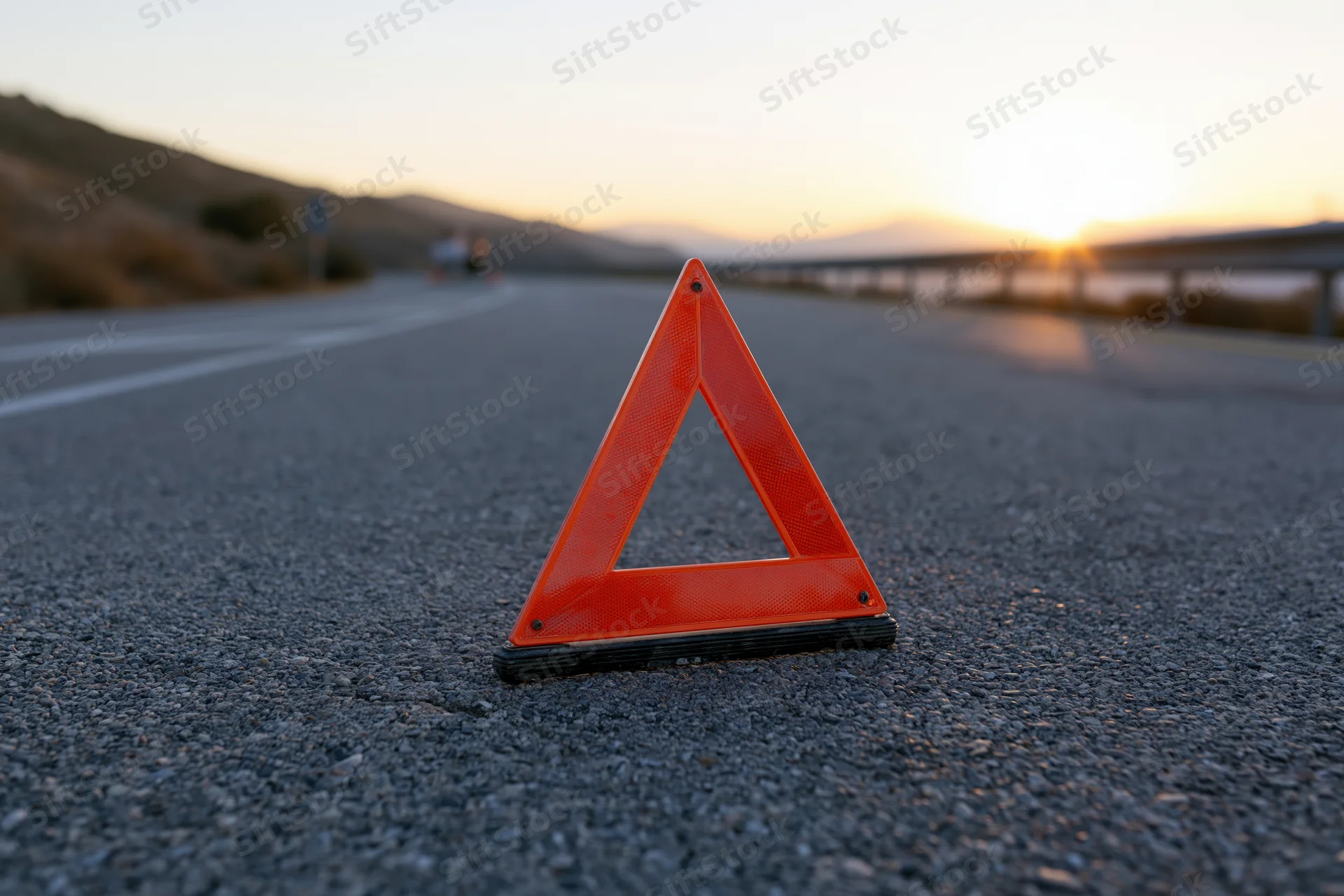Red emergency warning triangle on asphalt road at sunset