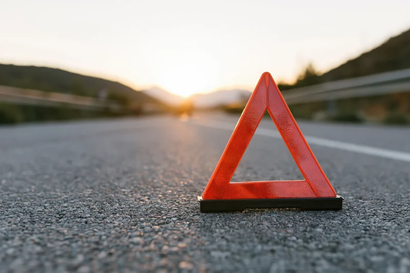 Red emergency warning triangle on asphalt road at sunset