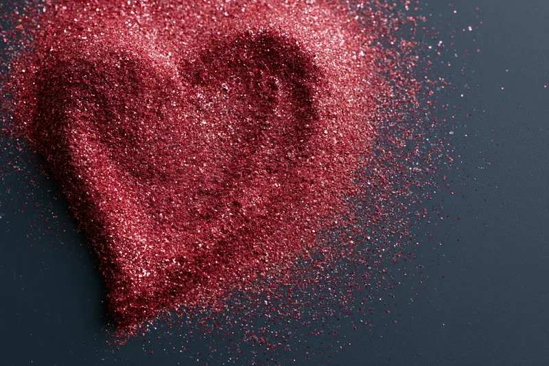 Red glitter scattered in rough heart shape on dark matte surface