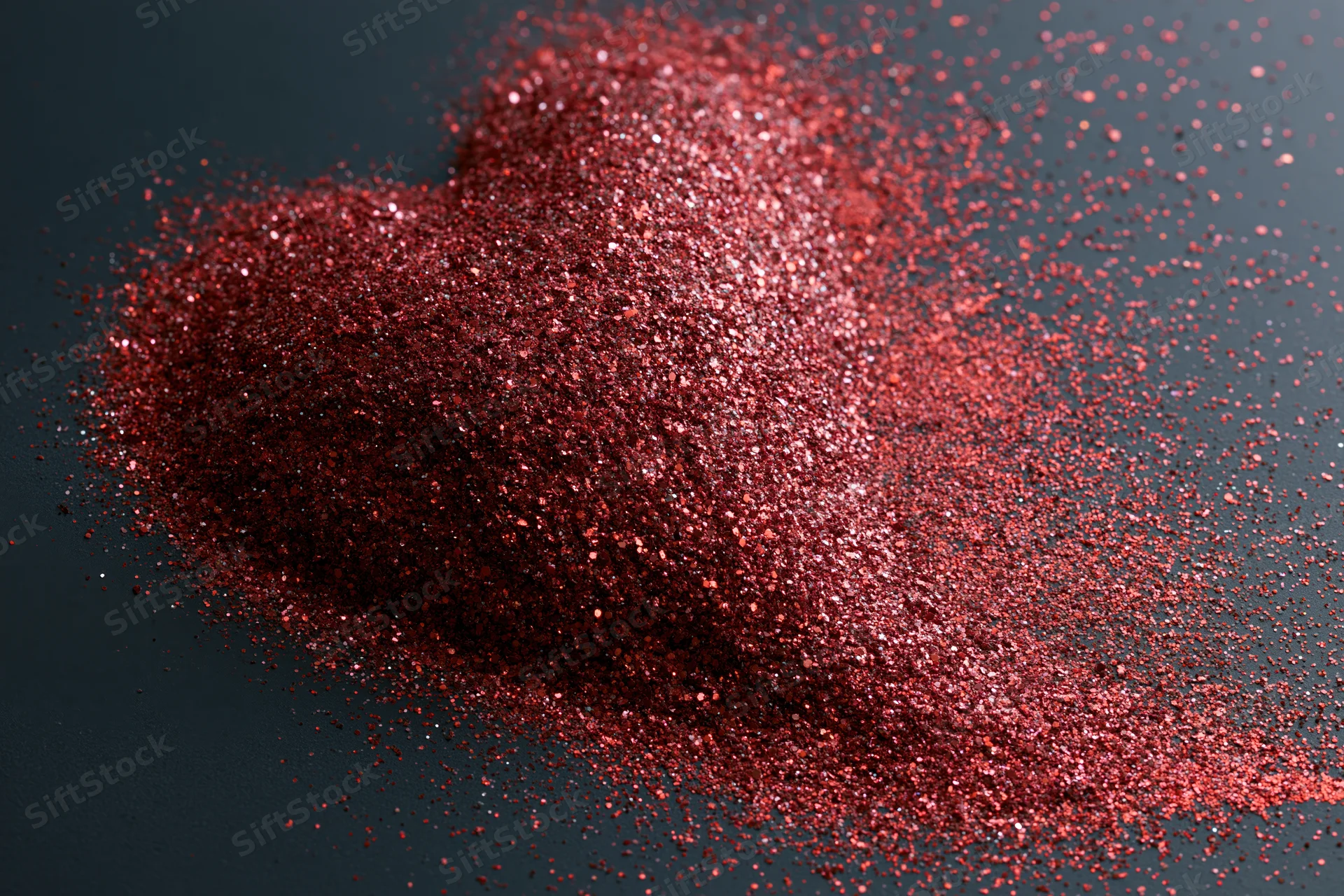 Red glitter scattered into a rough heart shape on a dark matte surface