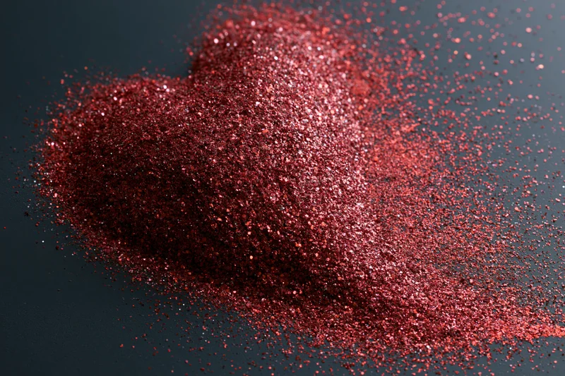 Red glitter scattered into a rough heart shape on a dark matte surface