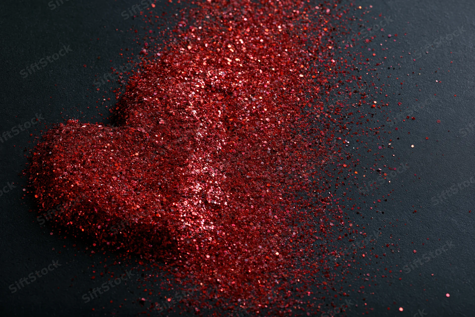 Red glitter scattered in rough heart shape on black matte surface