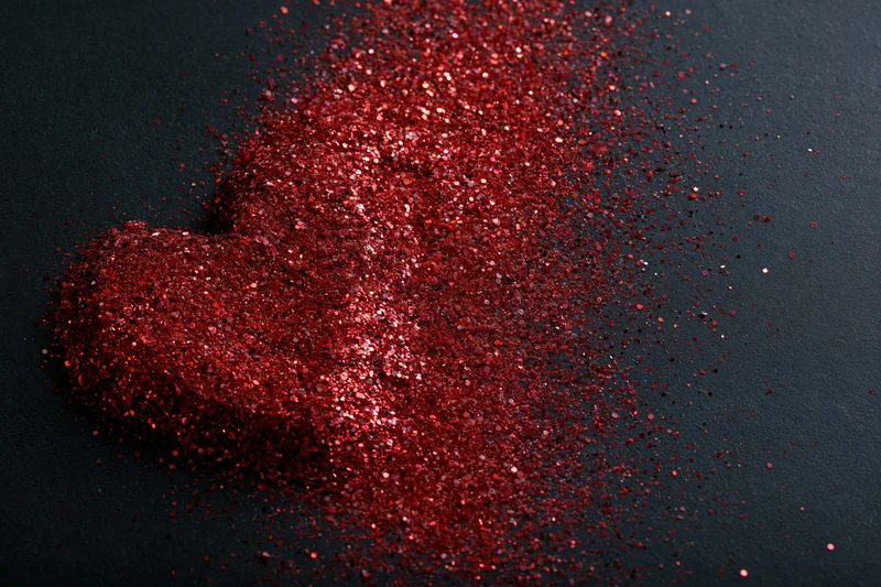 Red glitter scattered in rough heart shape on black matte surface
