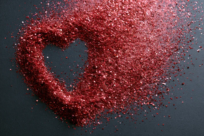 Red glitter scattered in rough heart shape on matte black surface