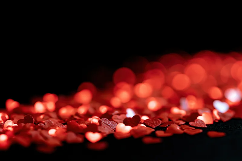 Red heart-shaped bokeh lights scattered across a dark background