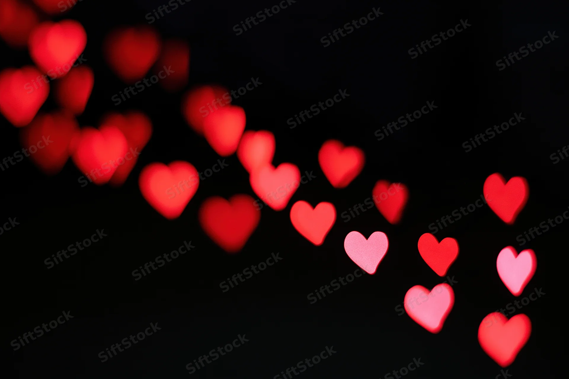 Red heart-shaped bokeh lights scattered across a black background with copyspace