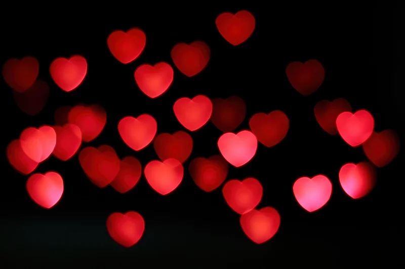 Red heart-shaped bokeh lights scattered across a black background